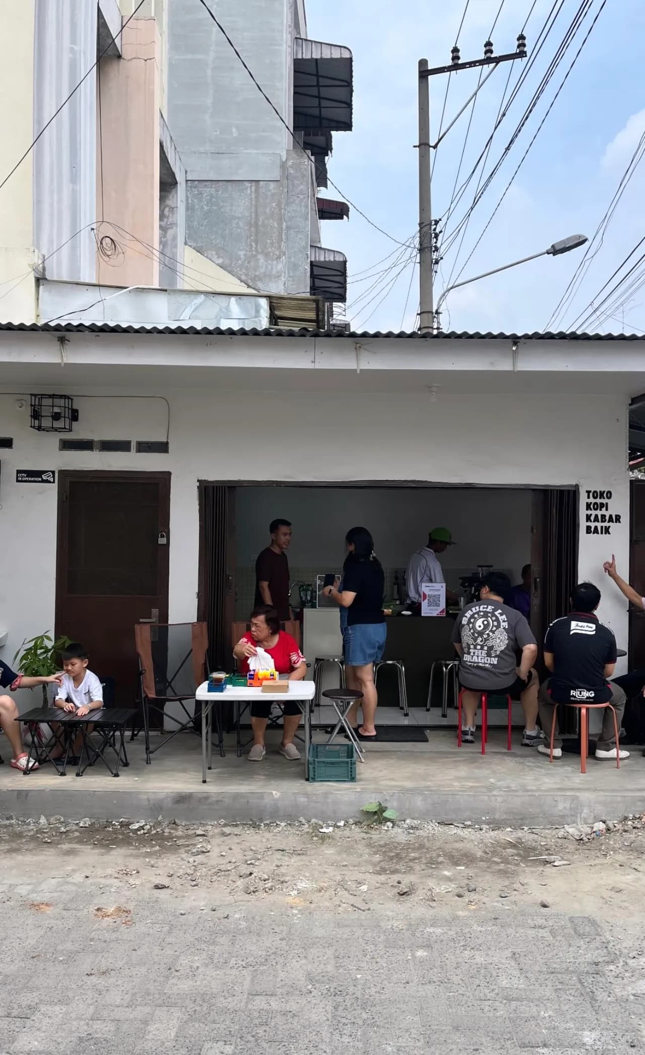 Suasana ramai di teras toko, keluarga dan tamu lintas usia menikmati kopi bersama