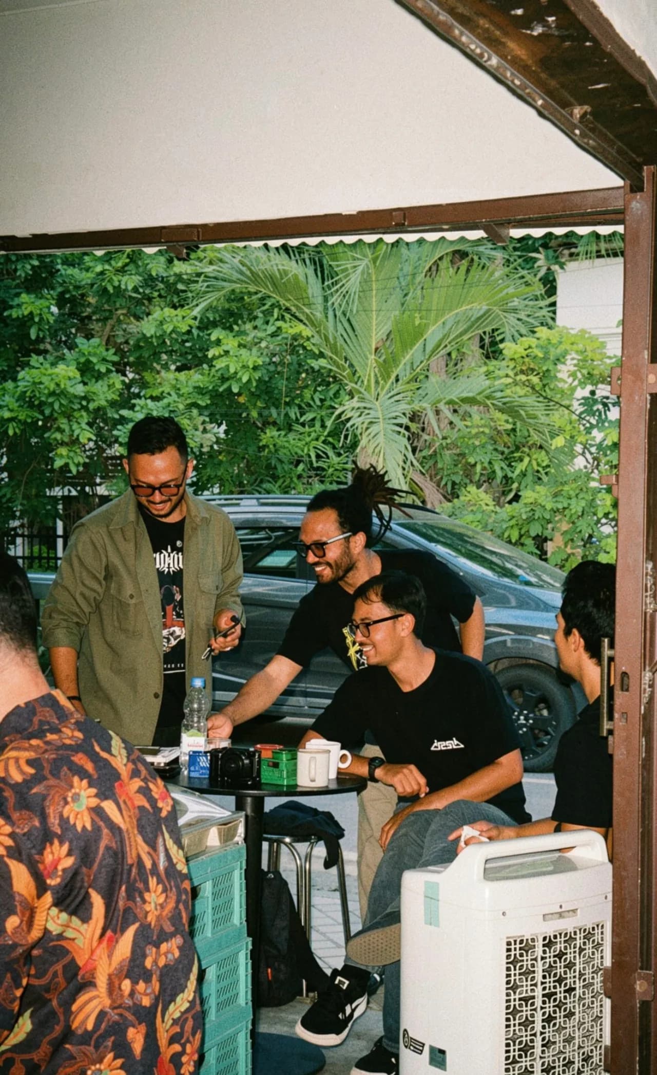 Tamu tertawa lepas saat ngobrol di meja kecil — momen hangat di Toko Kopi Kabar Baik